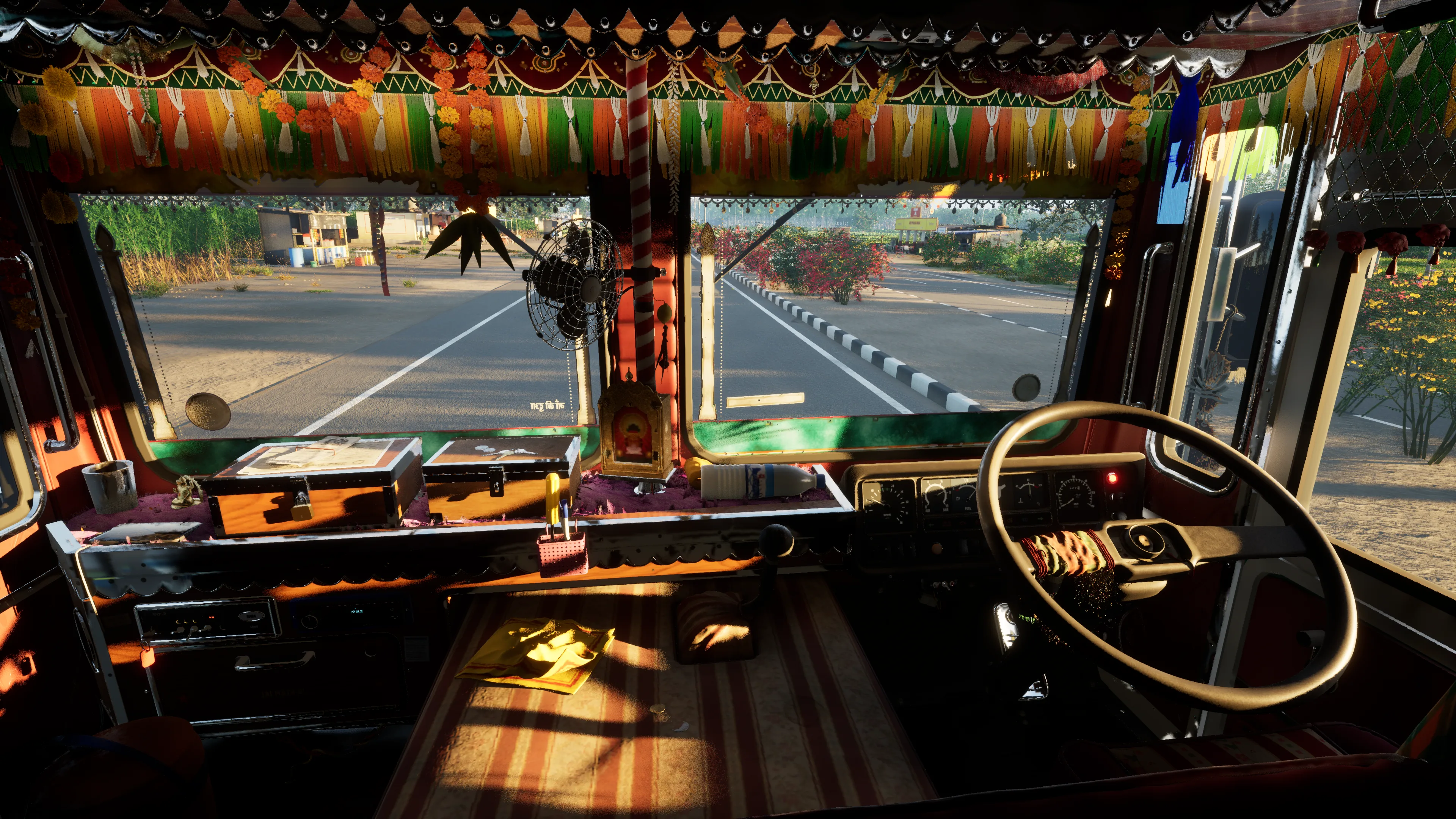 Low sun through the windscreen across the decorated dash, with a small shrine, a fan and a fringe of tassels, seen from behind the seats
