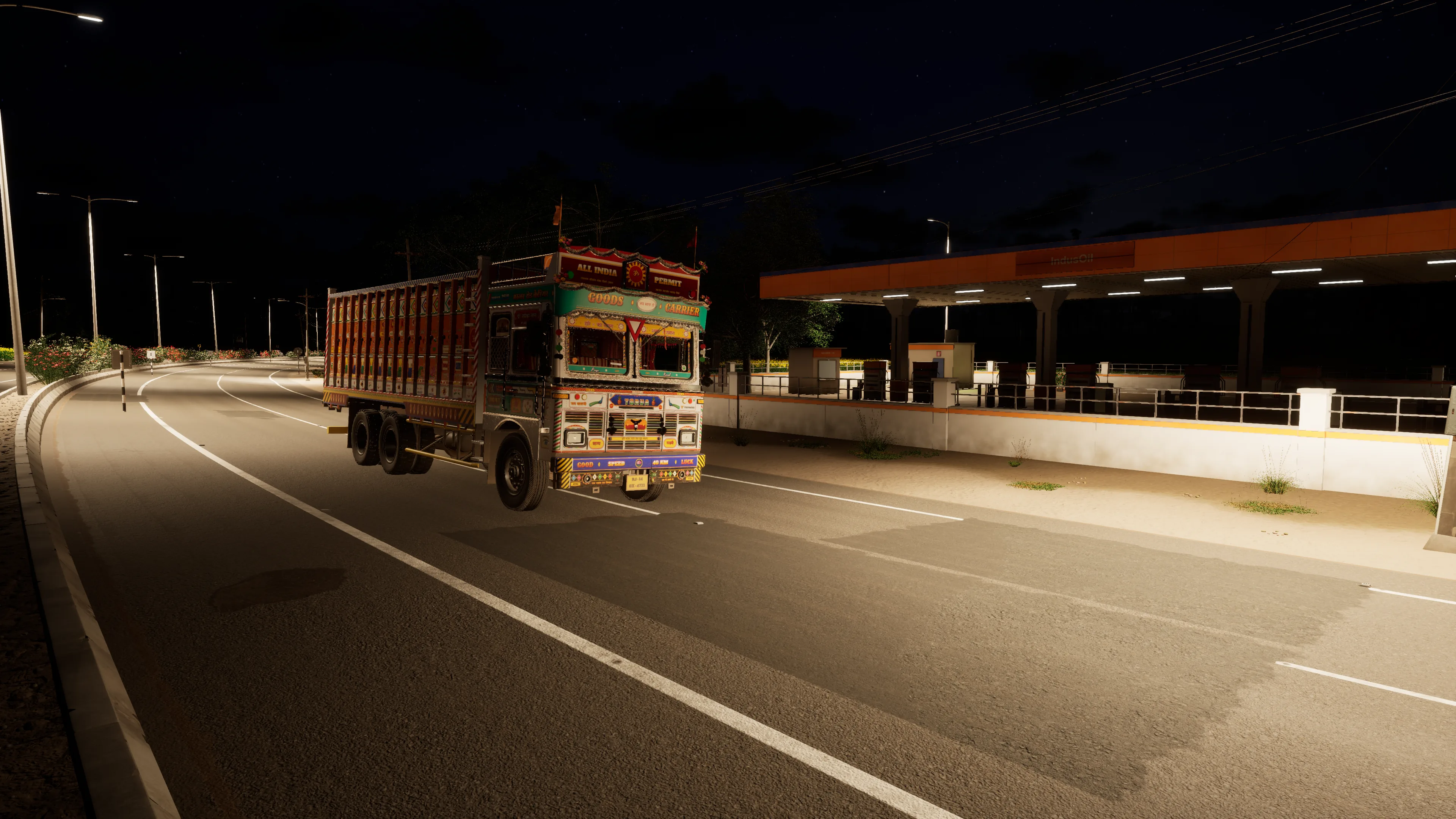A painted truck on a curving, streetlit highway at night, passing a fuel station with lights under its canopy