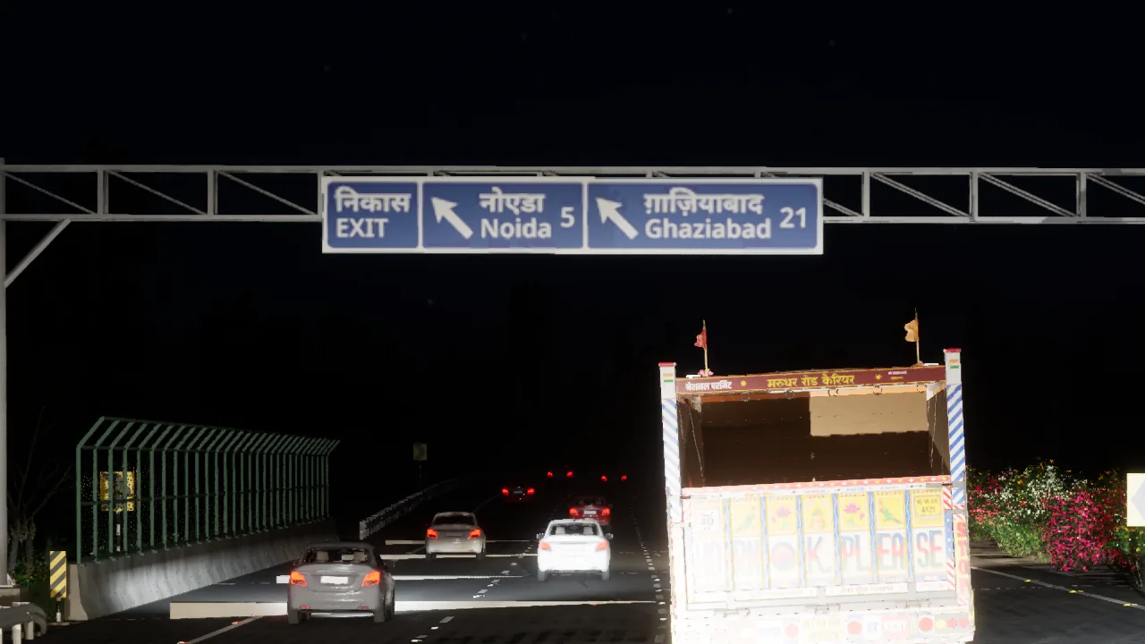 An overhead gantry at night on an expressway, the blue sign reading Exit, Noida 5 and Ghaziabad 21 in Hindi and English